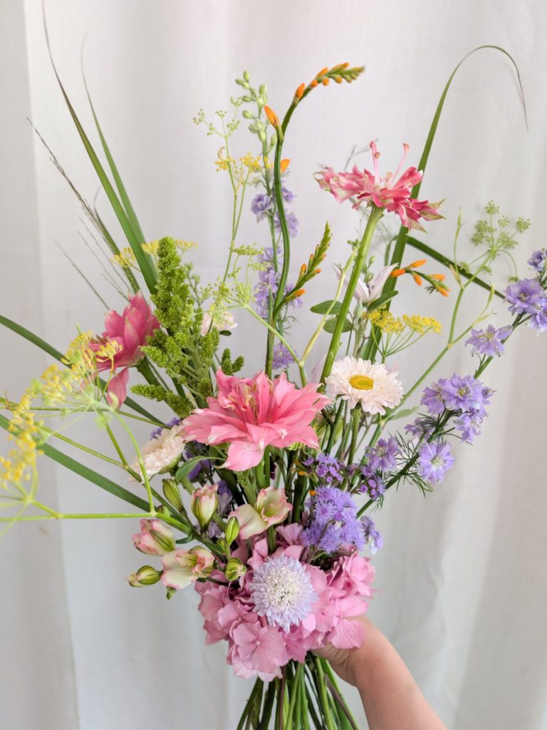 Brautstrauß Braut hält einen bunten Blumenstrauß mit blauem, rosa und weißem Blumenschmuck.